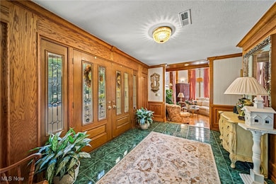 Foyer featuring dark tile patterned floors, a textured ceiling, a wainscoted wall, and crown molding