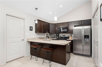 Kitchen with appliances with stainless steel finishes, dark brown cabinetry, a breakfast bar, light stone counters, and decorative light fixtures