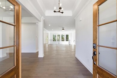 Corridor with dark wood finished floors, a raised ceiling, a chandelier, and ornamental molding