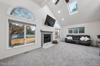 Carpeted living room featuring high vaulted ceiling, a skylight, plenty of natural light, recessed lighting, and a ceiling fan