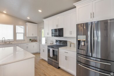 Kitchen with vaulted ceiling, stainless steel appliances, light wood finished floors, white cabinets, and recessed lighting