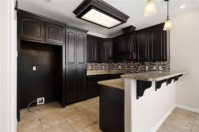 Kitchen with a breakfast bar, light tile patterned flooring, kitchen peninsula, hanging light fixtures, and backsplash