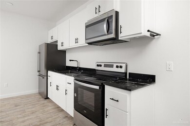 Kitchen featuring a sink, stainless steel appliances, light wood finished floors, white cabinetry, and baseboards