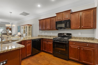 Kitchen with ornamental molding, black appliances, light stone countertops, light wood-style flooring, and a chandelier