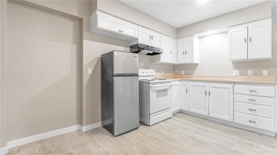 Kitchen with freestanding refrigerator, white electric stove, light countertops, and white cabinets