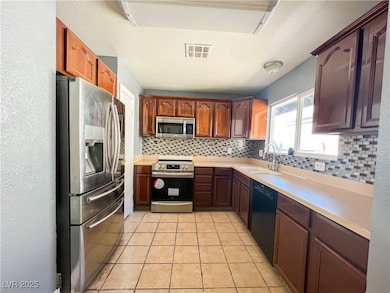 Kitchen with decorative backsplash, visible vents, a sink, light countertops, and stainless steel appliances