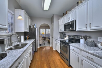 Kitchen featuring arched walkways, dark wood-style flooring, stainless steel appliances, white cabinetry, and a sink