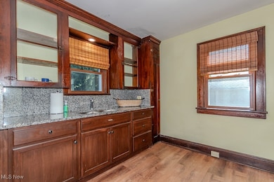 Kitchen featuring light wood-type flooring, light stone counters, backsplash, and glass insert cabinets