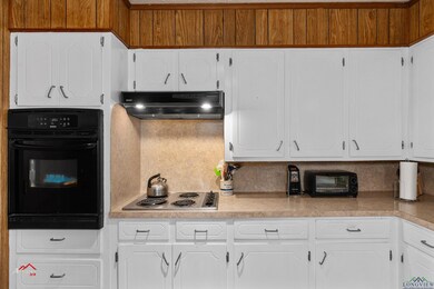 Kitchen with white cabinetry, stovetop, black oven
