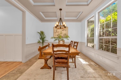 Dining room featuring a chandelier, a decorative wall, coffered ceiling, wainscoting, and crown molding