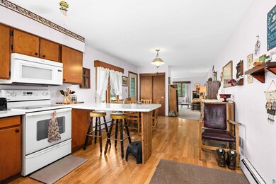 Kitchen with white appliances, baseboard heating, a peninsula, light wood finished floors, and light countertops