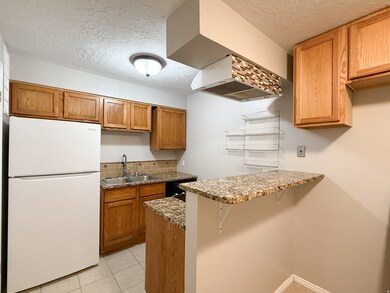 Kitchen featuring freestanding refrigerator, a textured ceiling, light stone countertops, a kitchen bar, and tasteful backsplash
