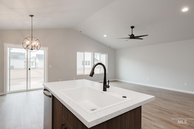 Kitchen featuring dark brown cabinetry, light wood finished floors, light countertops, open floor plan, and vaulted ceiling