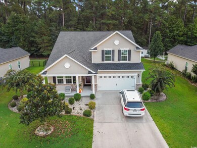Traditional-style home with a front yard, a porch, driveway, an attached garage, and roof with shingles