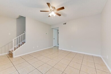 Empty room with a textured ceiling, light tile patterned floors, a ceiling fan, and stairs
