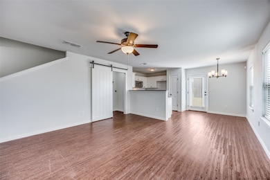 Unfurnished living room featuring ceiling fan, a barn door, a chandelier, and dark wood-type flooring