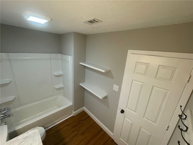 Full bath featuring a textured ceiling, wood finished floors, and washtub / shower combination
