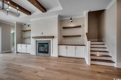 Unfurnished living room with ornamental molding, light wood finished floors, beamed ceiling, stairway, and a large fireplace