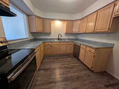 Kitchen featuring appliances with stainless steel finishes, range hood, a textured ceiling, dark wood-style flooring, and light brown cabinets