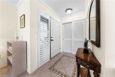 Entrance foyer with light tile patterned floors, crown molding, inlaid floor details, and a textured ceiling