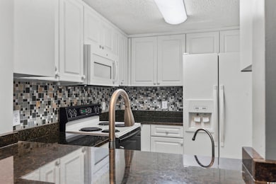 Kitchen featuring white cabinetry, white appliances, dark stone countertops, and a textured ceiling
