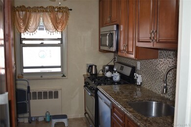 Kitchen with appliances with stainless steel finishes, tasteful backsplash, dark stone countertops, light tile patterned floors, and radiator heating unit