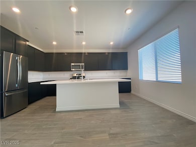 Kitchen featuring appliances with stainless steel finishes, dark cabinets, a kitchen island with sink, recessed lighting, and light wood finished floors