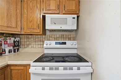 Kitchen with white appliances, light countertops, brown cabinetry, and decorative backsplash