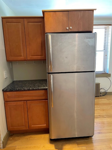 Kitchen featuring freestanding refrigerator, brown cabinets, light wood finished floors, and dark stone countertops