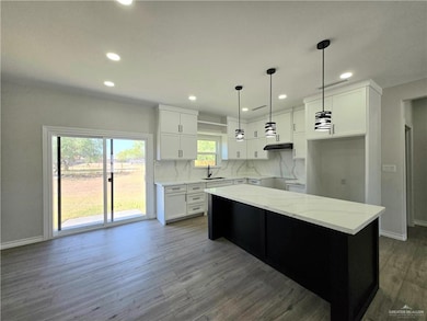 Kitchen featuring dark cabinets, decorative backsplash, white cabinetry, decorative light fixtures, and light stone counters