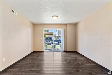 Empty room featuring a textured ceiling and dark wood-style flooring