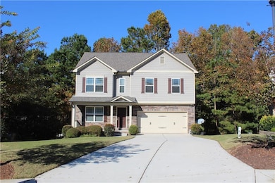 View of front of house with stone siding, a porch, a front lawn, concrete driveway, and view of wooded area