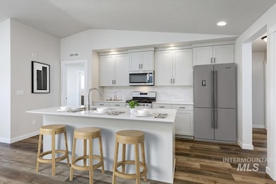 Kitchen with stainless steel appliances, vaulted ceiling, a breakfast bar, decorative backsplash, and dark wood-style flooring