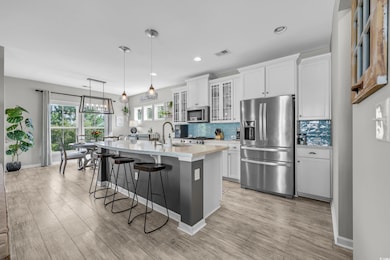 Kitchen featuring stainless steel appliances, light countertops, a kitchen island with sink, a breakfast bar area, and tasteful backsplash