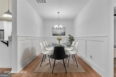 Dining room featuring a decorative wall, wood finished floors, a wainscoted wall, and a chandelier