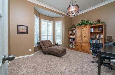 To the left of the foyer, the spacious study features a bay window dressed with Plantation shutters, glass paneled French doors, custom painted walls, double crown molding, neutral frieze carpet, and a modern light fixture with Edison bulbs.