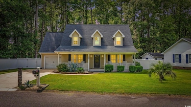 Cape cod-style house featuring roof with shingles, covered porch, concrete driveway, an attached garage, and view of scattered trees