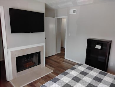 Bedroom with dark wood-style floors and a fireplace with raised hearth