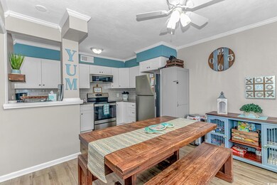 Kitchen with tasteful backsplash, appliances with stainless steel finishes, white cabinetry, ornamental molding, and light wood-style flooring