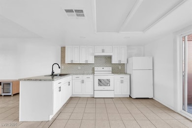 Kitchen featuring white appliances, tasteful backsplash, light tile patterned floors, a peninsula, and white cabinets