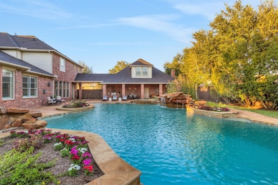 Expansive 80,000-gallon resort-style pool featuring a 12-foot deep end with natural stone diving rock, cascading waterfalls, relaxing spa, and lush tropical landscaping—your private backyard paradise.