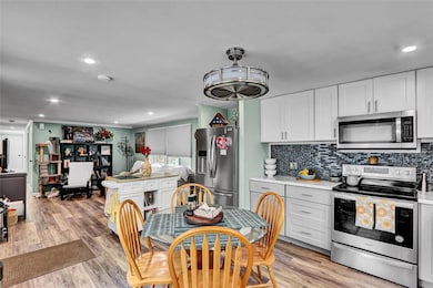 Kitchen with appliances with stainless steel finishes, backsplash, light countertops, white cabinets, and light wood finished floors
