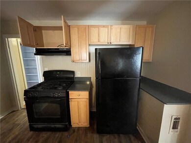 Kitchen with black appliances, under cabinet range hood, dark countertops, dark wood-style flooring, and light brown cabinetry