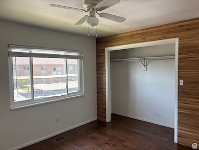 Unfurnished bedroom featuring wooden walls, multiple windows, a closet, dark wood-style floors, and a ceiling fan