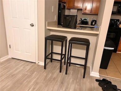 Kitchen with a breakfast bar area, light countertops, black appliances, light wood-style floors, and brown cabinets