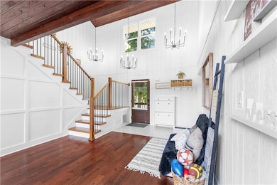 Entryway featuring a chandelier, stairway, a decorative wall, plenty of natural light, and beam ceiling