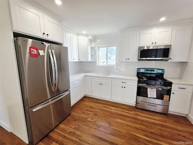 Kitchen featuring appliances with stainless steel finishes, white cabinets, open shelves, decorative backsplash, and dark wood-style flooring
