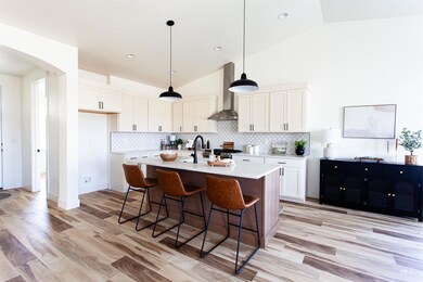 Kitchen featuring wall chimney exhaust hood, light countertops, light wood-style floors, arched walkways, and white cabinets