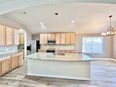 Kitchen with arched walkways, light brown cabinetry, tasteful backsplash, light stone countertops, and pendant lighting