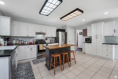 Kitchen with decorative backsplash, stainless steel appliances, recessed lighting, a kitchen breakfast bar, and light tile patterned floors